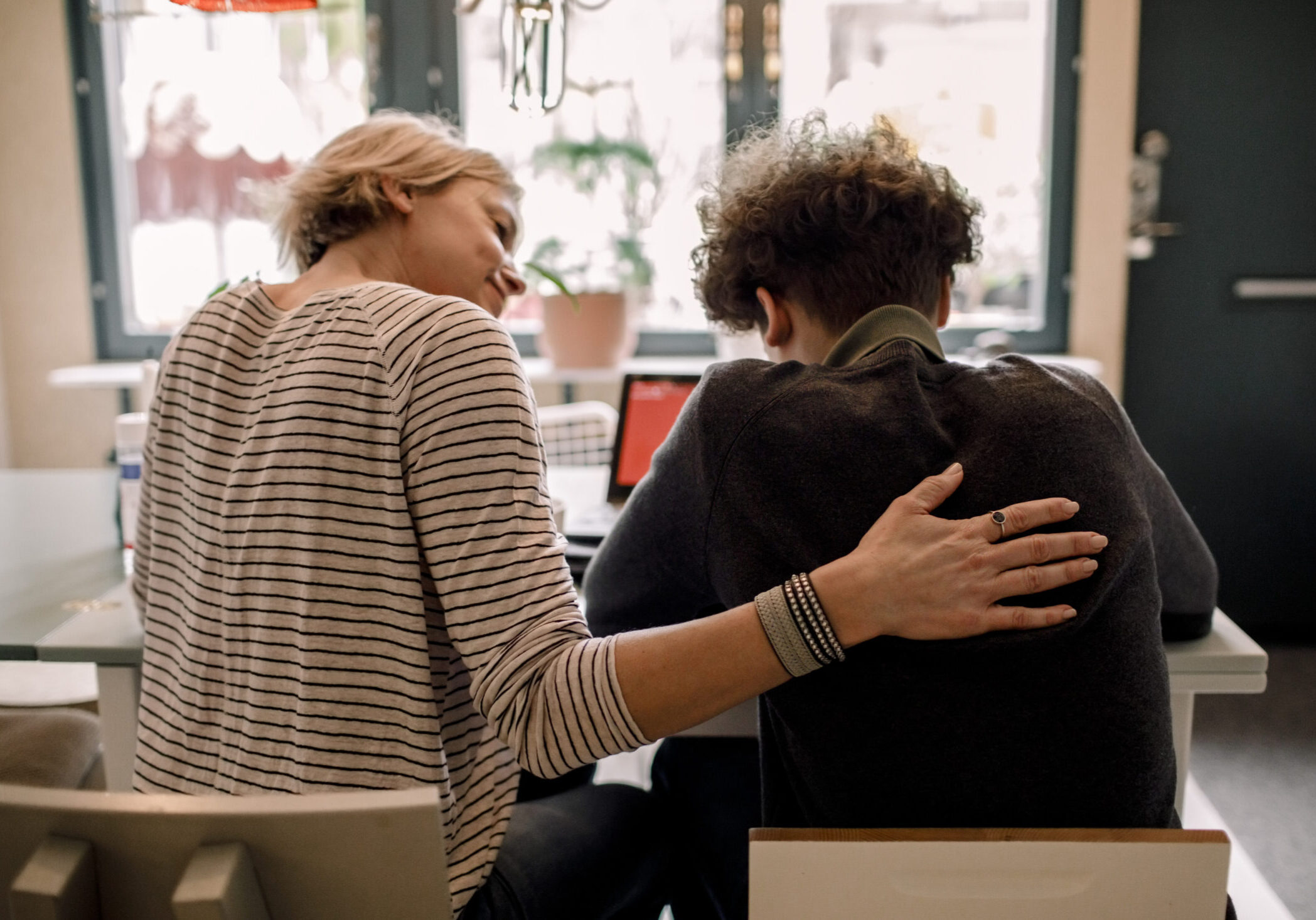 Mother sitting by teenage son studying at home