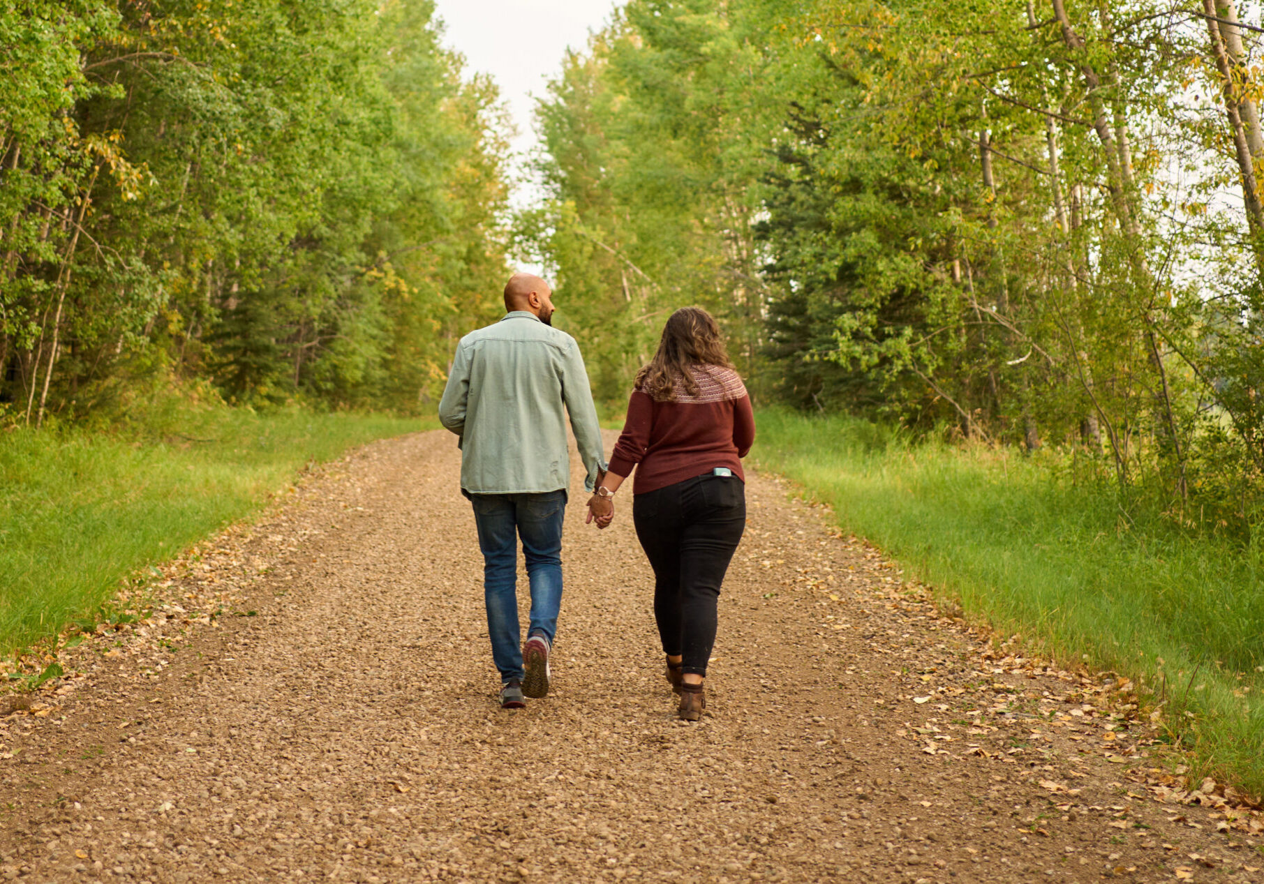 Couple walking hand in hand on a road through a forest Rear view of a young couple walking hand in hand together along a dirt road through a forest to their cabin