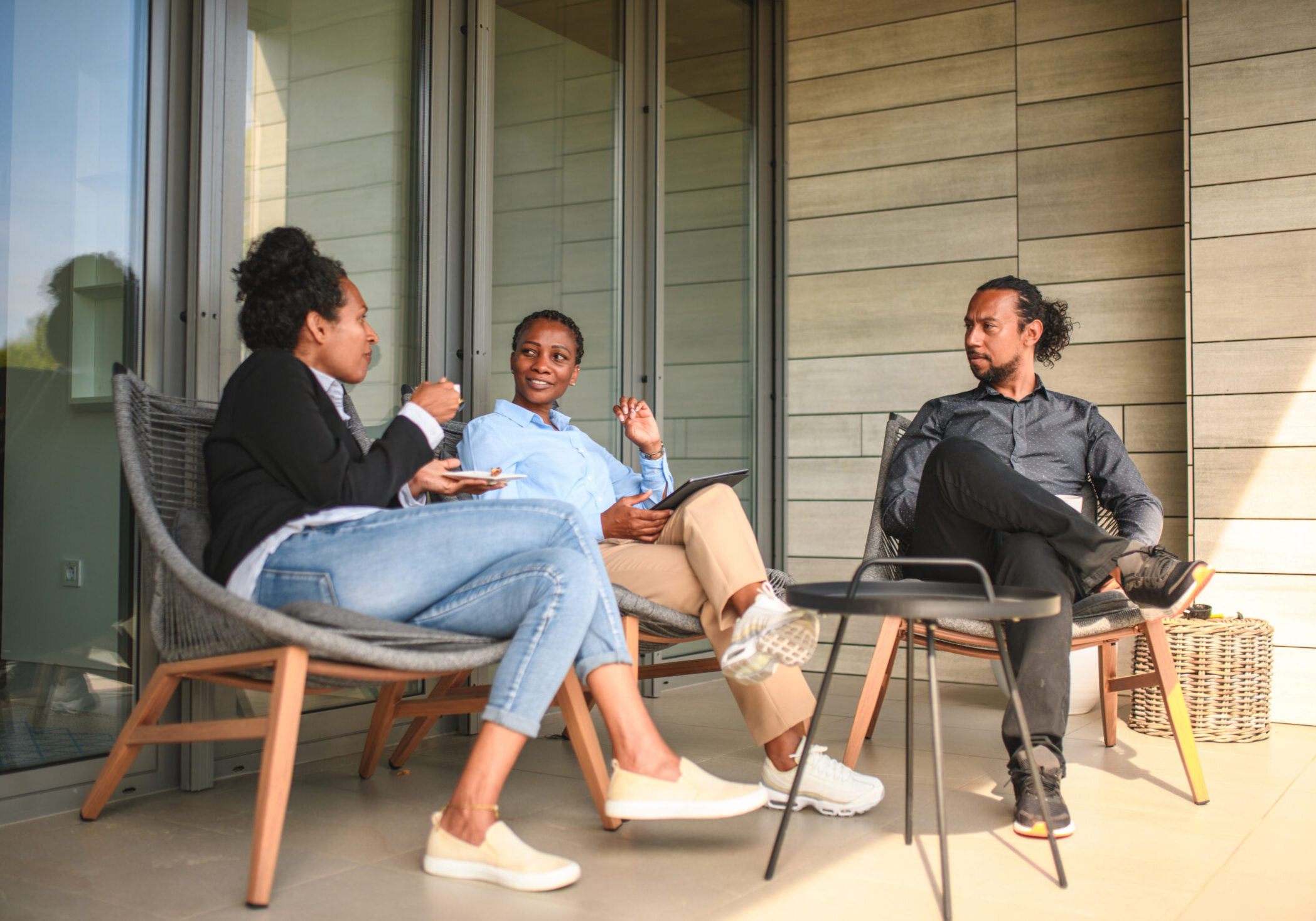 Mixed Race Colleagues Drinking Coffee On A Terrace During After Work Multiracial business strategists drinking coffee on a terrace. They are sitting around a small table on the terrace of a business building.